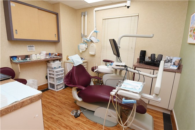 A treatment room at the practice, with a dental chair, overhead light, monitor and instrument tray.